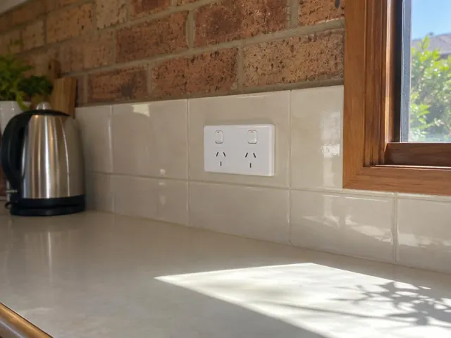 White double power point on tiled kitchen splashback above a bench with brick wall and timber window trim in San Remo