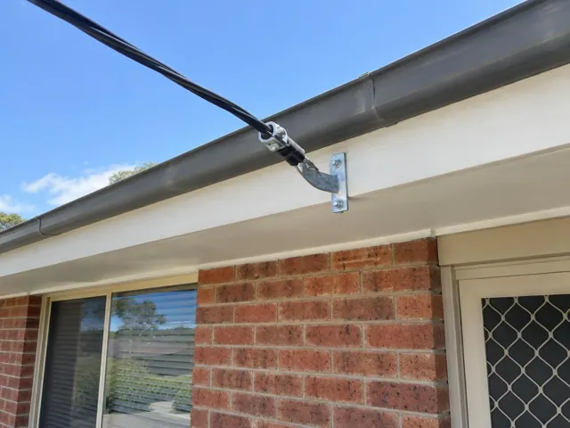 Overhead service cable and point-of-attachment bracket on a brick house eave in Lake Haven
