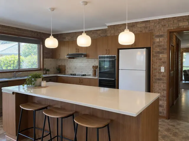 Kitchen with three pendant lights over a stone island in a brick and wood interior in Charmhaven